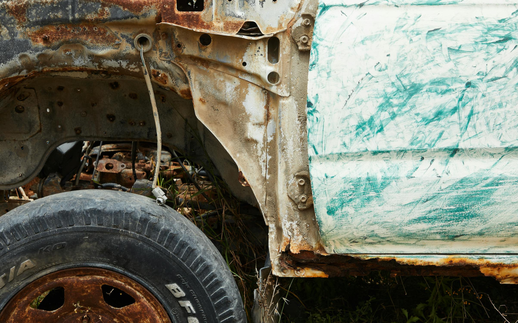 Close-up of a rusty, damaged car in a yard.