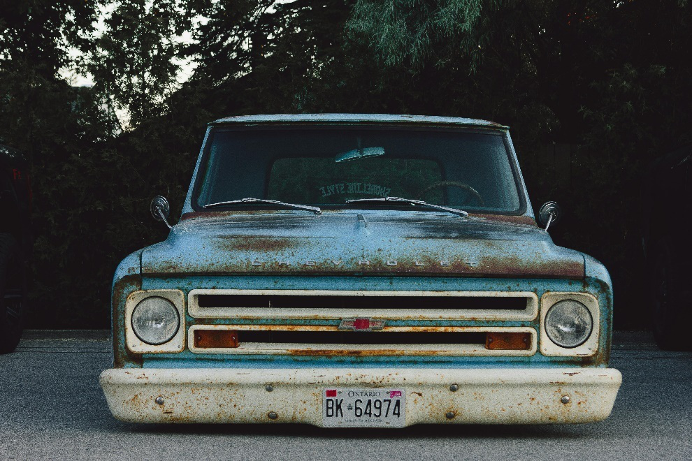 An old blue car rusting away on the road